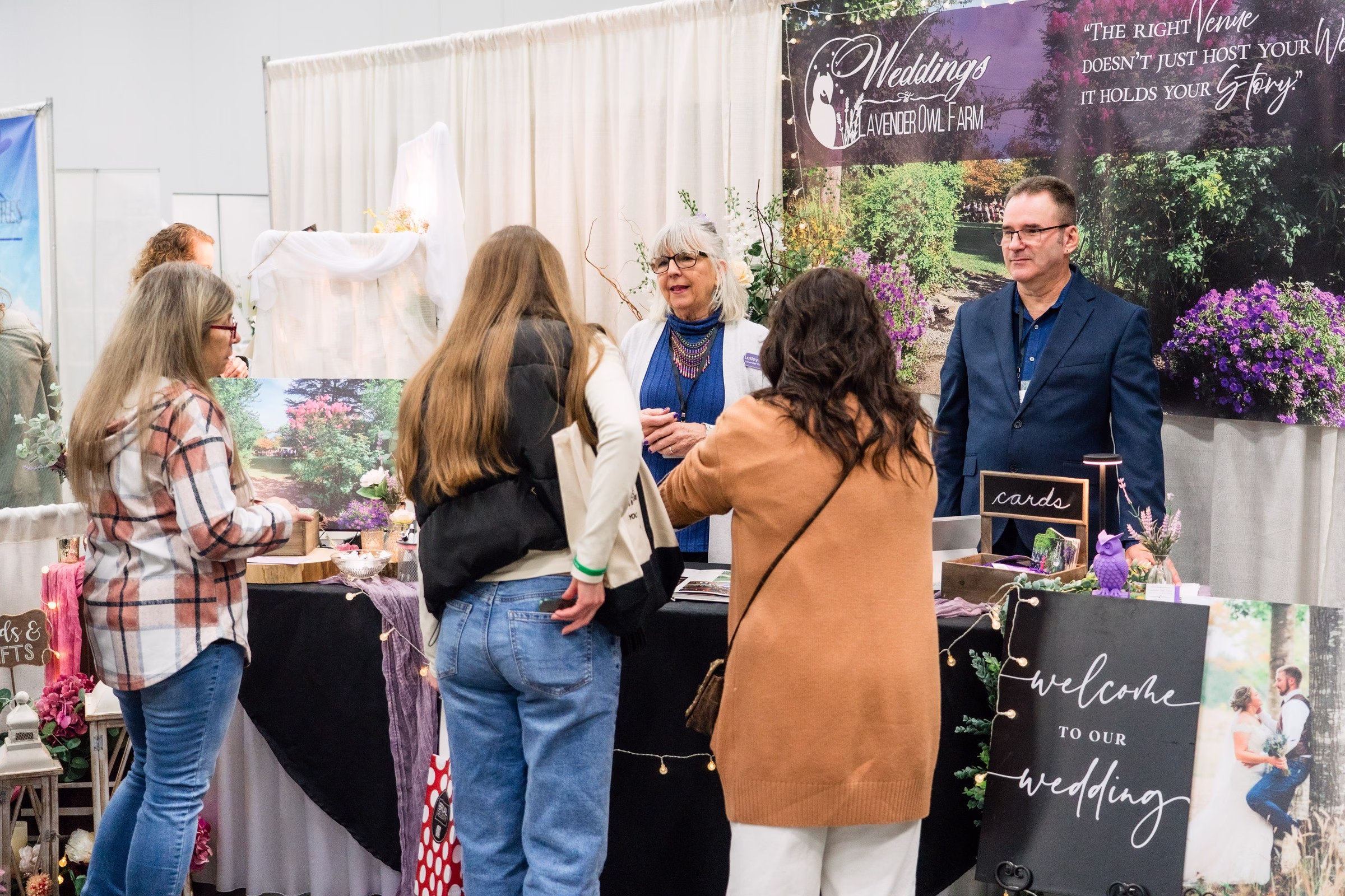 Weddings at Lavender Owl Farm venue booth at Salem Wedding Show with visitors viewing wedding displays and talking with venue representatives